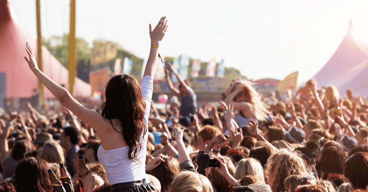 A diverse crowd of people enjoying a lively music festival, with colorful lights and a stage in the background.