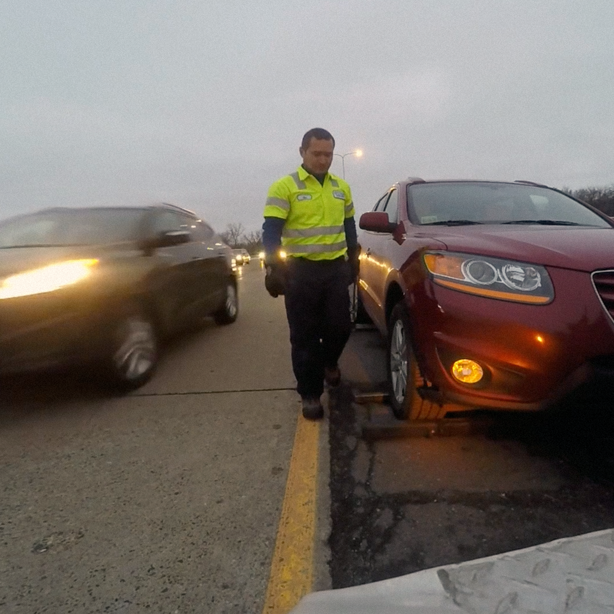 roadside worker walks towards stalled car on side of highway