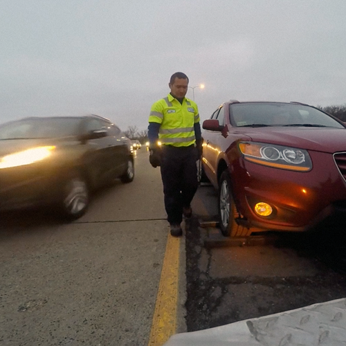 roadside responder walks towards stalled car on side of highway