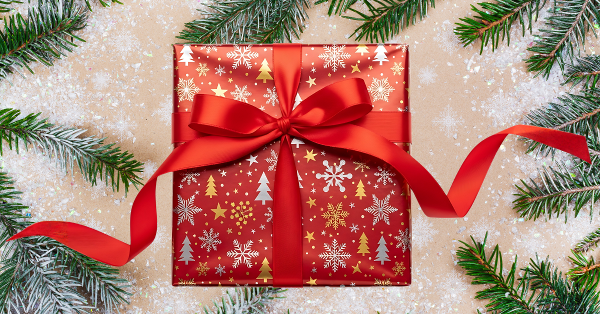 picture of holiday gift wrapped with bow and holiday branches in background