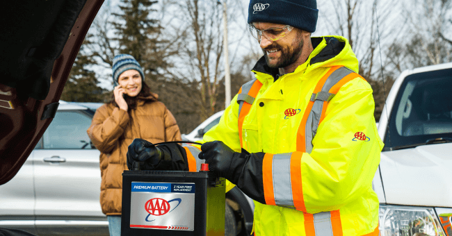 A AAA Roadside Technician replacing a battery while a member looks on