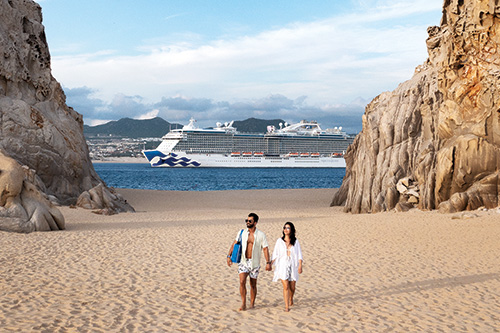 couple walk on beach with cruise ship in background
